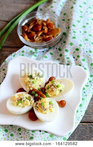 Delicious deviled eggs on a plate. Boiled eggs stuffed with grated cheese, marinated mushrooms and fresh green onions. Interesting appetizer recipe with eggs and mushrooms. Vertical photo