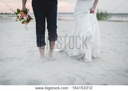 Bride and groom walk on the beach. Cropped image