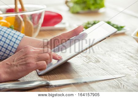 Close-up partial view of woman using digital tablet in kitchen