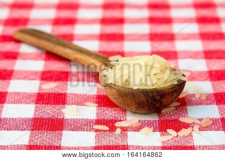 Raw parboiled rice in a wooden spoon on checkered tablecloth