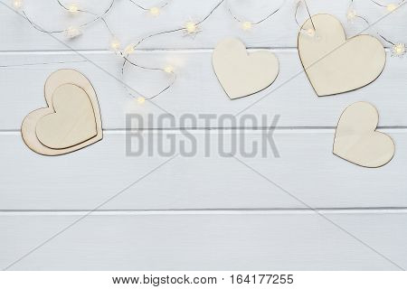 Overhead view of wooden love Valentine's hearts with lite fairy lights over a wooden background with copy space available.