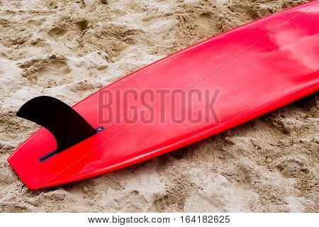 Red surfboard with black fin laying flat on sand