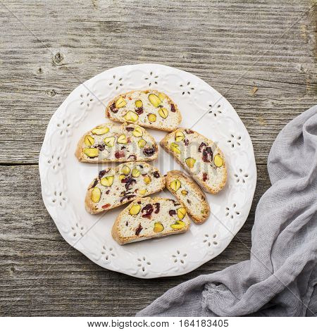 Crispy traditional delicious Italian biscotti cookies or kantuchchi with pistachios and dried cranberries in a glass on wooden background. selective