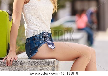 Travel adventure teenage journey concept. Attracitve woman wearing denim shorts and white top sitting next to her green suitcase relaxing after arrival
