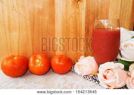 A glass of fresh cold tomato juice pink roses tomatoes on wooden background idea of healthy beverage