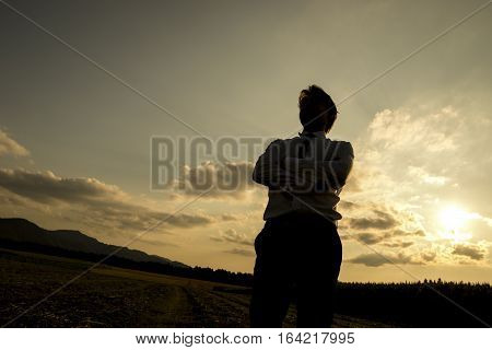 Silhouette of a man at sunset standing with folded arms and his back to the glowing sun low angle with copy space.