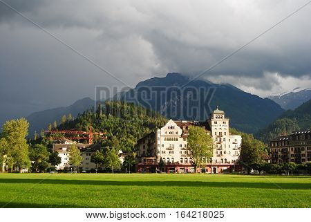 Interlaken, Switzerland - July 13, 2014. Street view along Alpenstrasse in Interlaken, with commercial buildings, construction cranes, grass lawn and mountains in the distance, at dusk.