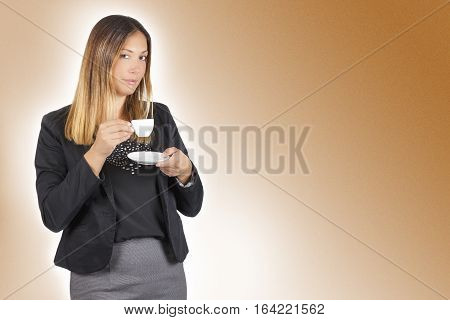 Business woman drinking coffee in cup. Work pause. A standing woman having a coffee during her coffee break. The beautiful young woman is drinking holding a small white cup of coffee.