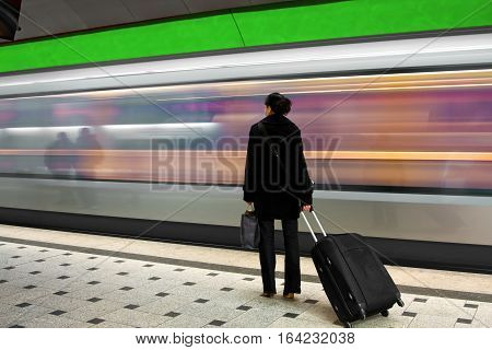 young woman waiting for the subway and carrying a handbag and a rolley. image is brightly colored, subway has strong motion blur.