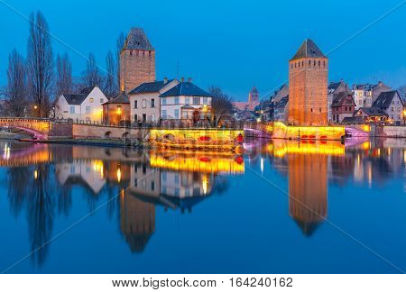 Medieval towers and bridges Ponts Couverts with mirror reflections in Petite France during twilight blue hour, Strasbourg, Alsace, France