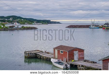 Little red shack on a dock in the small village and community of Twillingate, Newfoundland.  Maritime homes along the cove shoreline in this coastal village with docked boats and dories.
