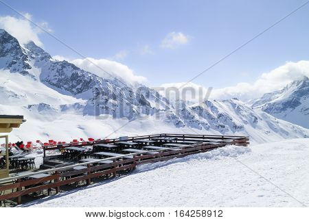 Apres ski chalet restaurant with chairs and tables outside facing snowy mountain peaks and slopes Les Arcs Alps Paradiski France