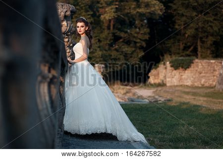 bridal female walking in ancient castle; beautiful stylish bride in luxury wedding dress at sunset;