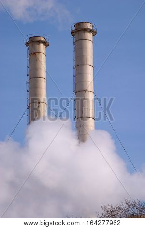 Two industrial smoke pipes and white steam over blue sky