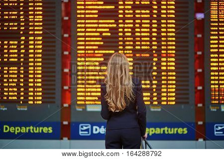 Woman With Hand Luggage In International Airport Terminal, Looking At Information Board