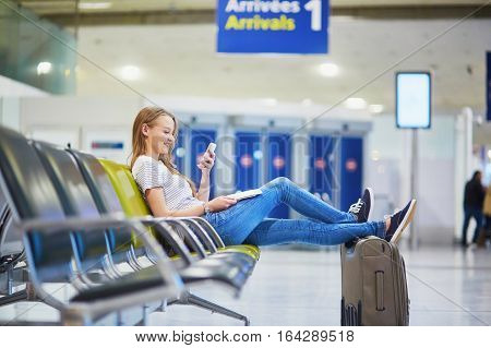 Young Travelerin International Airport Checking Her Mobile Phone While Waiting For Her Flight