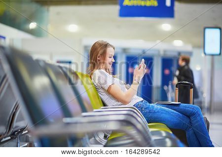 Young Travelerin International Airport Checking Her Mobile Phone While Waiting For Her Flight