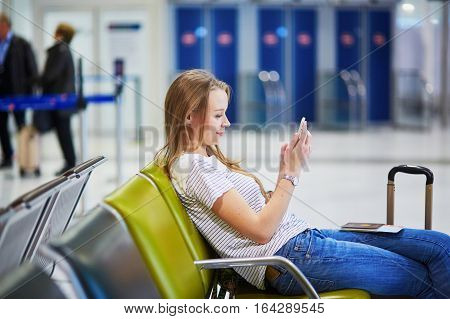 Young Travelerin International Airport Checking Her Mobile Phone While Waiting For Her Flight
