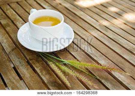 Cup of tea & group of Cenchrus setaceus grass flowers on wooden table with blurry bokeh in the background. Have a lot of text space for your project.
