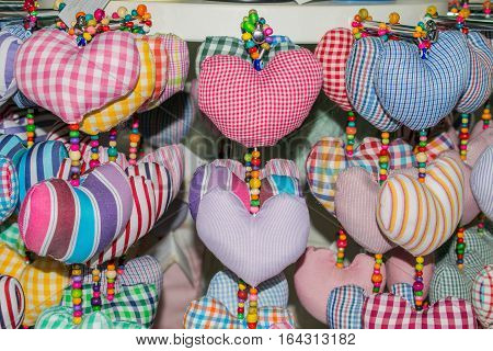 A lot of soft toys in the form of hearts from a bright and colorful fabric