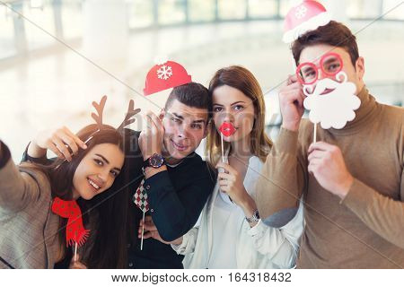 Young friends having fun holding winter artificial mustache and lips stick making selfie photo