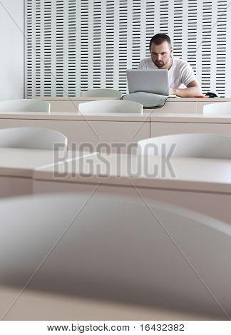 Junge männliche College-Studenten, die Arbeiten auf seinem Laptopcomputer in einem Klassenzimmer