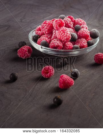 Frozen raspberries in a glass saucer. Frost on the berries. Dark background.