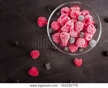 Frozen raspberries in a glass saucer. Frost on the berries. Dark background.