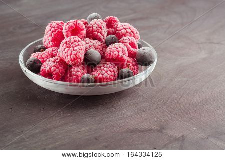 Frozen raspberries in a glass saucer. Frost on the berries. Dark background.