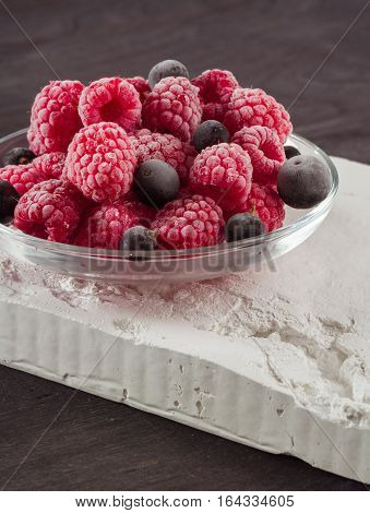 Frozen raspberries in a glass saucer. Frost on the berries. Dark background.