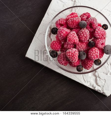 Frozen raspberries in a glass saucer. Frost on the berries. Dark background.