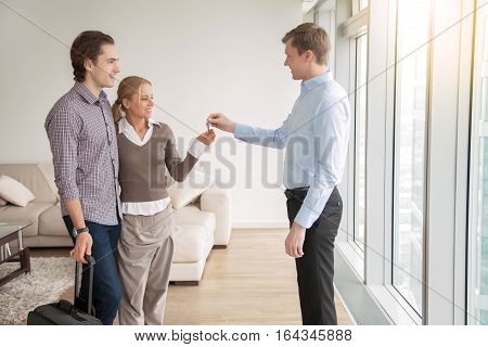 Young attractive married couple in love buying or renting new apartment, meeting with real estate agent, occupiers moving into rented accommodation, starting family life, moving out from another city