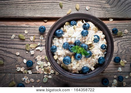 Oatmeal with blueberries,  coconat and seeds at rustic wooden table. Flat lay.