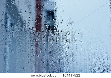 Window glass with condensation, strong, high humidity in the room, large water droplets flow down the window, cold tone, natural water drops on window