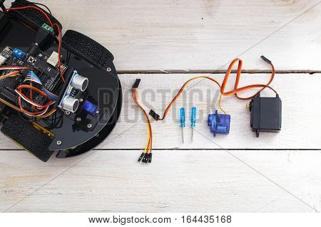 parts for the robot assembly. Screwdrivers,  servo, wires on a white wooden table. View from above