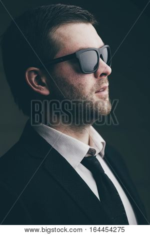 Portrait of a young trendy man in sunglasses in a dark room close up