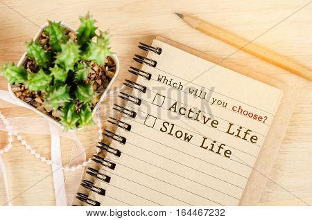 Whick will you Choose? Active life or Slow life in notebook with cactus on wooden background. Conceptual between active life and slow life