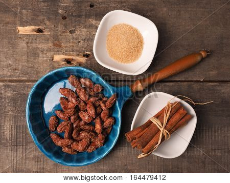 Tasty roasted almonds in a blue ceramic bowl with ingredients on wood