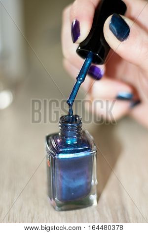 drop of dark green metalic nail varnish flowing down from the brush