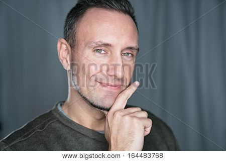 likeble young businessman smiles into camera while holding his chin