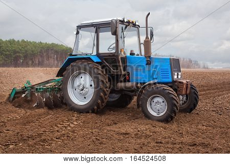 In the earlyspring morning tractor goes and pulls a plowplowing a field before landing of crops. On the earth dry stalks of a last year's sunflower lie.