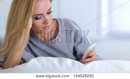 Pretty woman in her living room lying on the couch sending message.