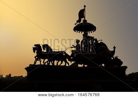 An ornamental statute of people riding a carrage is silhouetted against the evening sunlight in Rishikesh India.
