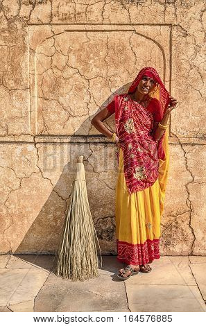 AMER, INDIA - NOVEMBER 18, 2016: An anonymous woman with a traditional broom stands against a wall in the Amber Fort in the city of Amer near Jaipur, India.