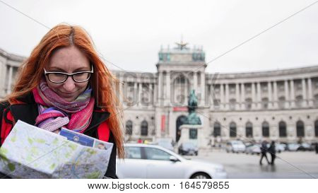 Yong tourist - woman with red hair and glasses looking map in Heldenplatz, Vienna, close up