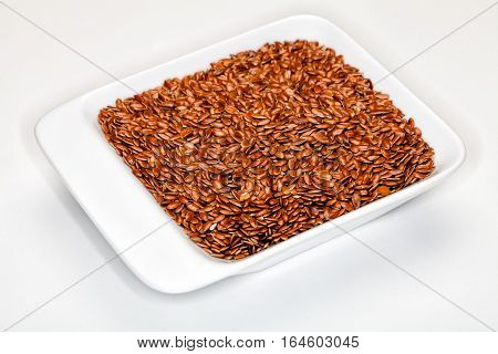 Flax, Flaxseeds. Flaxseed, in a white container. White background. One hundred grams of ground flaxseed supplies about 534 calories, 41 grams of fat, 28 grams of fiber, and 20 grams of protein. Image taken with macro lens.