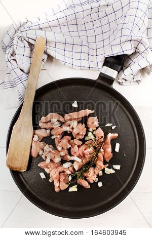raw chicken goulash with onion wooden spatula and thyme on a pan