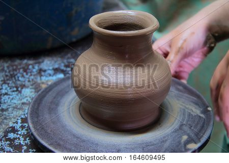 A clay pot on a pottery wheel, pottery craft, moulding the pot with your hands, sculpting hands