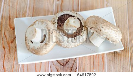 Mushrooms Champignon, Agaricus Bisporus On A White Plate, Close Up, Wood Background.