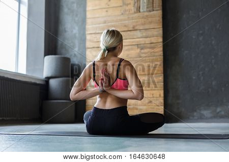 Young slim blond woman in yoga class making asana exercises. Girl do Reverse Prayer Pose, back and shoulders stretching. Healthy lifestyle in fitness club.